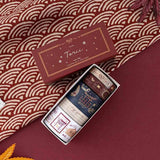 An opened box of Tsuki Torii washi tape set by notebook therapy laid out on red background with red traditional Japanese patterned fabric