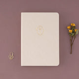 Bullet Journal notebook with gold key illustrated detail on the cover on linen with heart-shaped padlock paperclip and dried flowers on the side