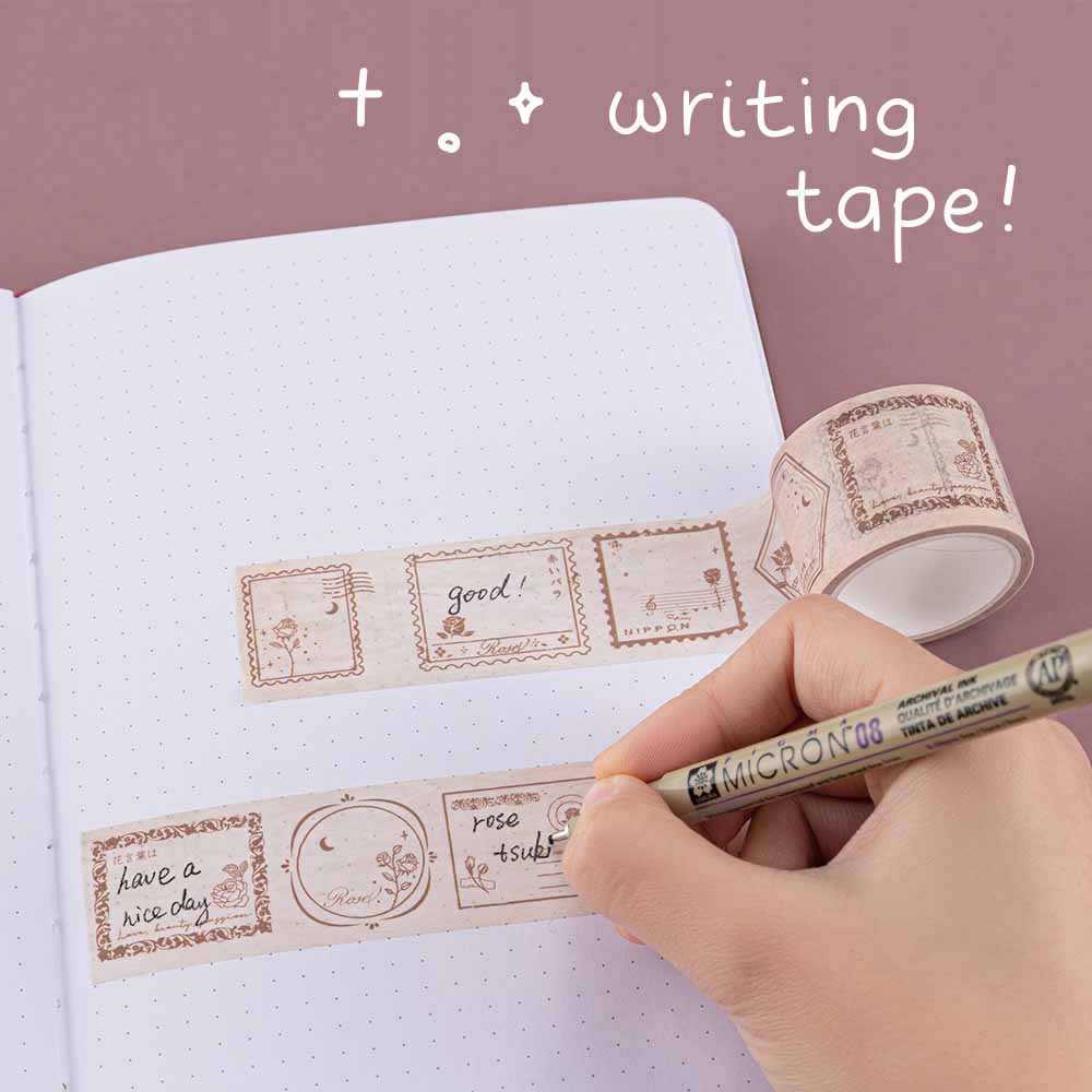 Tsuki ‘Vintage Rose’ Writing Washi Tape rolled out on Tsuki ‘Vintage Rose’ Limited Edition Bullet Journal with pen held in hand on mauve background