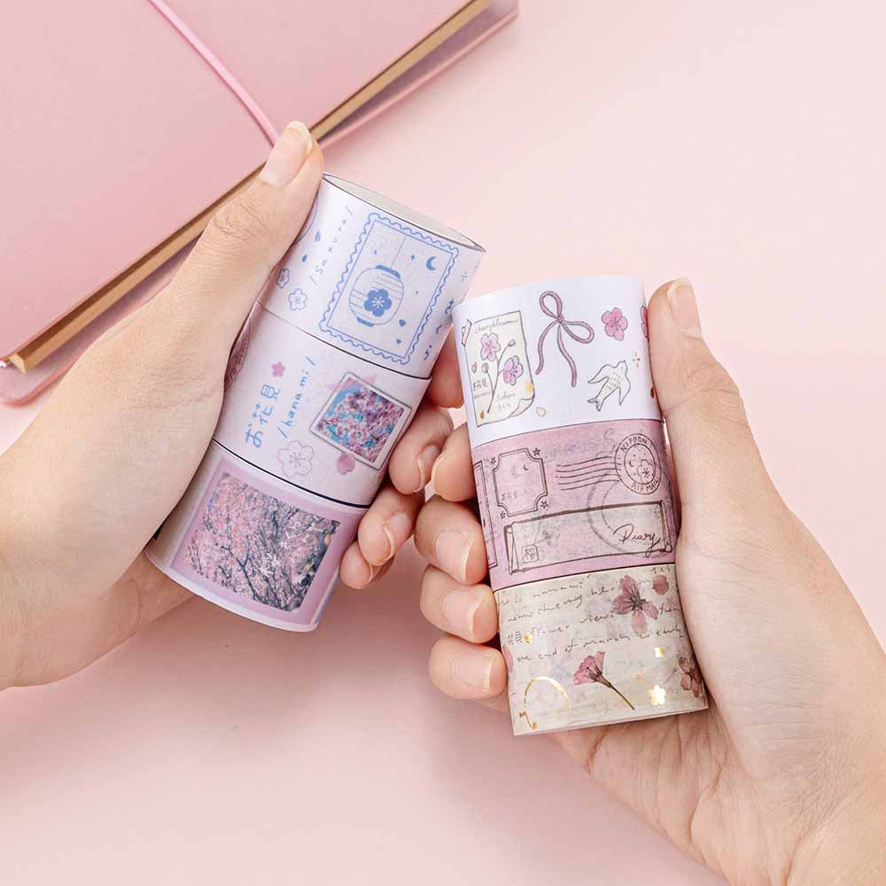 Tsuki ‘Sakura Journey’ Vintage Journal Washi Tape Set held in hands over Tsuki ‘Sakura Journey’ Limited Edition Travel Notebook on pink background