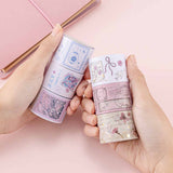 Tsuki ‘Sakura Journey’ Vintage Journal Washi Tape Set held in hands over Tsuki ‘Sakura Journey’ Limited Edition Travel Notebook on pink background
