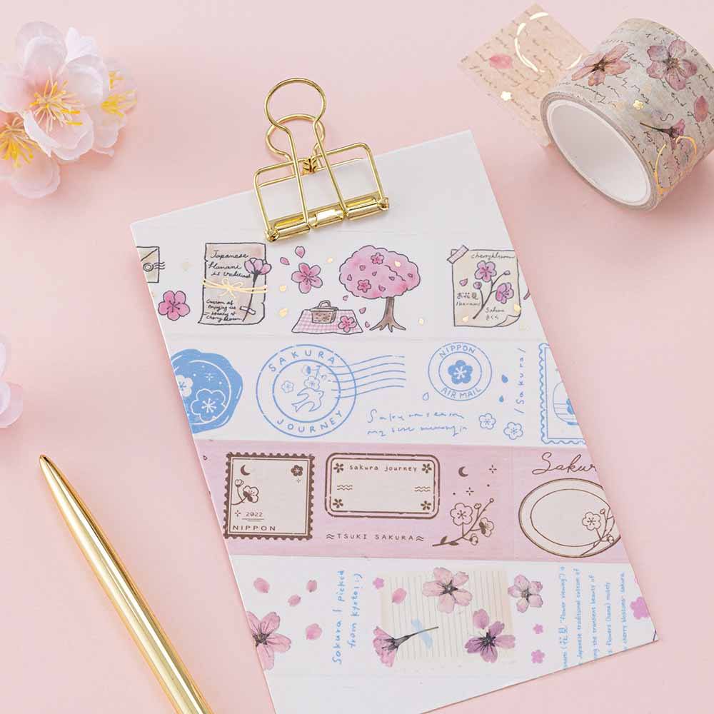 Tsuki ‘Sakura Journey’ Vintage Journal Washi Tape Set on white clipboard with gold pen and cherry blossoms on pink background