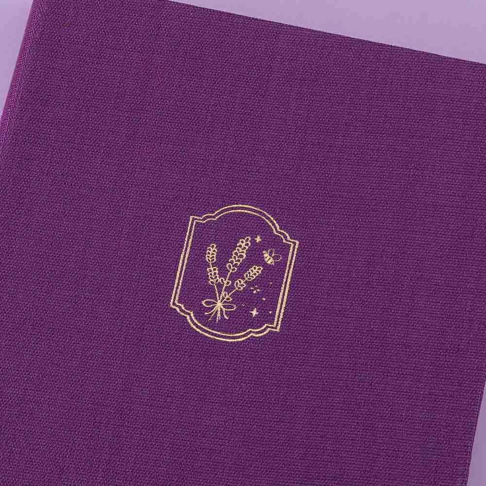 Tsuki ‘Enchanted Garden’ lavender foil design on purple linen bullet journal on purple background close up shot