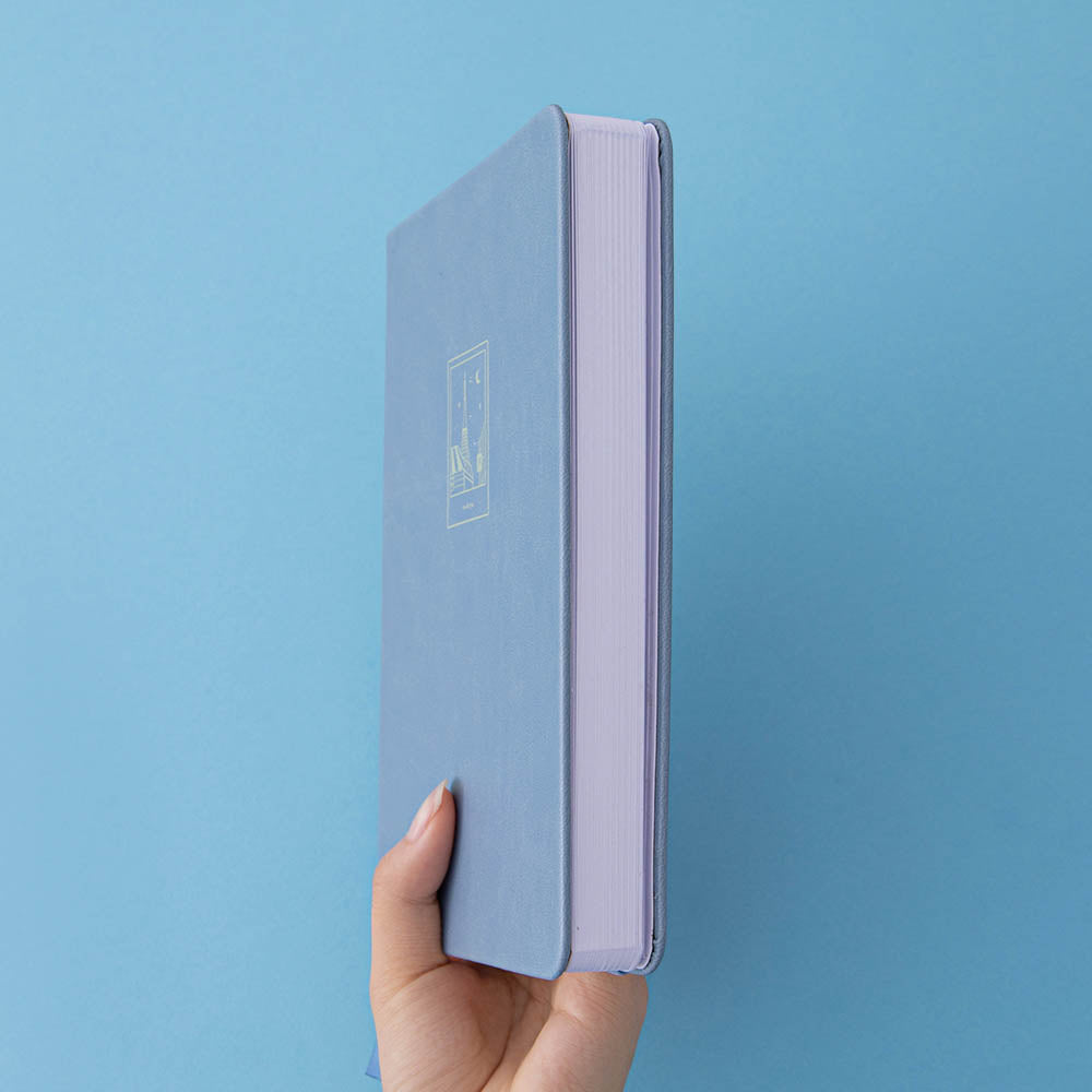 A hand holding a blue leather notebook showing the white page edges