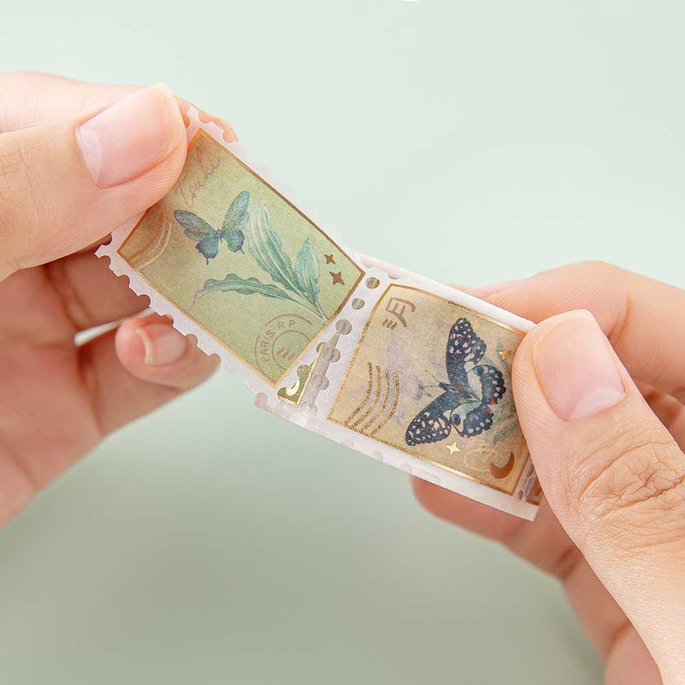 Close up of Tsuki ‘Flutter + Dream’ Stamp Washi Tape by Notebook Therapy x Pelinkan held in hands in mint background