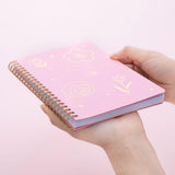 Tsuki sakura pink floral ringbound notebook held in hand at bottom angle in pink background