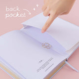Open back page pocket of Tsuki ‘Sakura Journey’ Limited Edition Bullet Journal held in hand with free bookmark gift on pink background