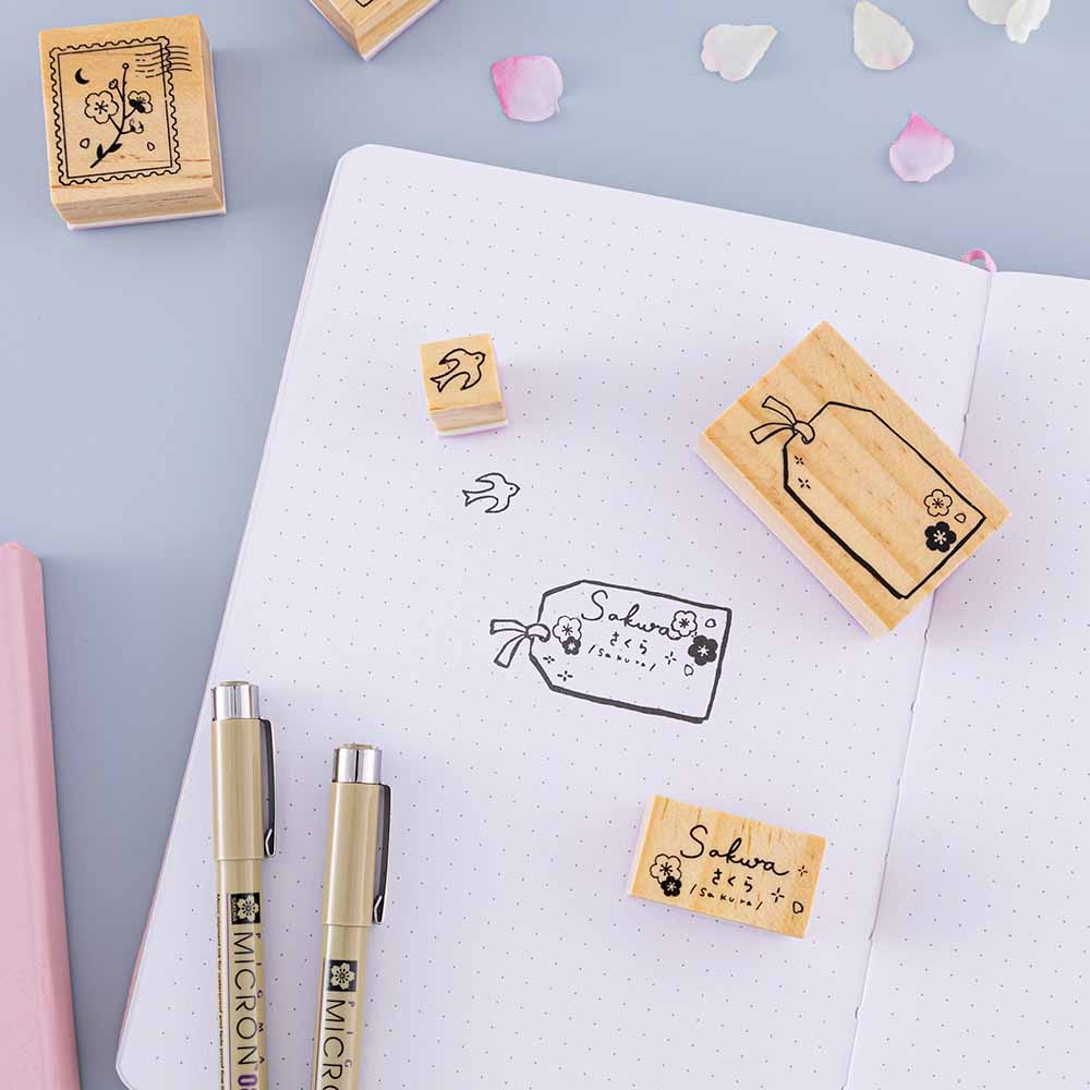 Tsuki ‘Sakura Journey’ Bullet Journal Stamp Set on open bullet journal page with pens and cherry blossom petals on light blue background
