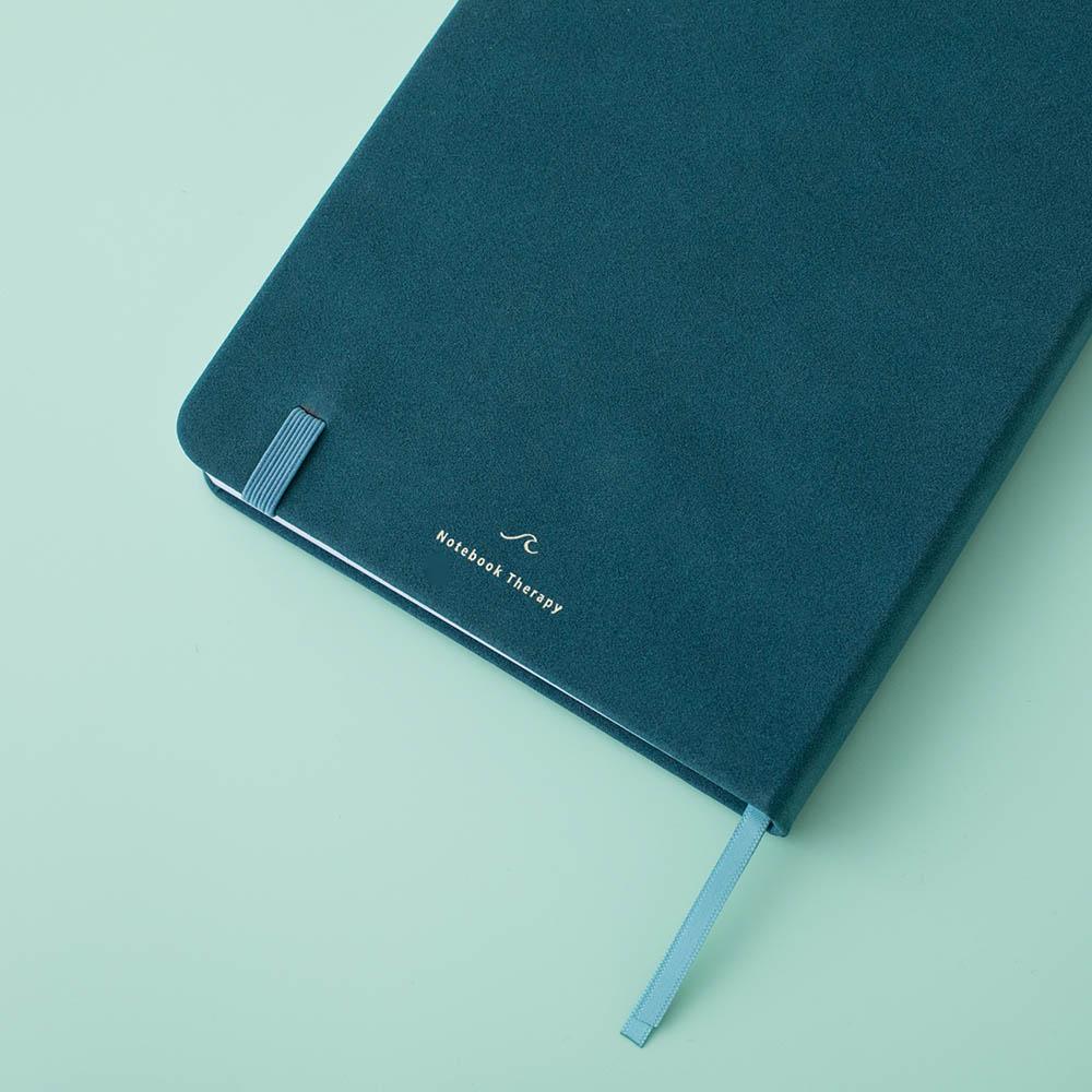 Close up of the back cover of Sea green velvet Tsuki Dolphin Days bullet journal on green background