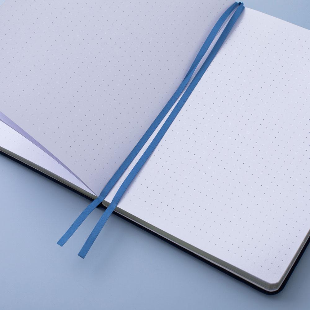 Deep blue textured vegan leather Tsuki Gentle Giant luxury edition bullet journal on open page with two bookmark ribbons on blue background