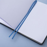 Deep blue textured vegan leather Tsuki Gentle Giant luxury edition bullet journal on open page with two bookmark ribbons on blue background