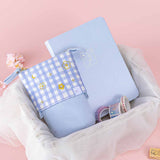 Tsuki ‘Sakura Journey’ Pop-Up Pencil Case with Tsuki ‘Sakura Journey’ Limited Edition Bullet Journal and Tsuki ‘Sakura Journey’ Washi Tapes in netted basket with cherry blossoms and Tsuki ‘Sakura Journey’ Bullet Journal Stamp on light pink background