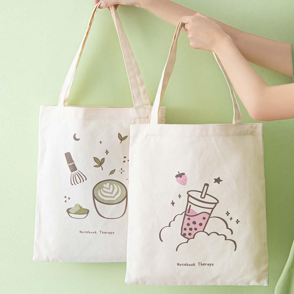 Tsuki ‘Matcha Matcha’ Tote Bag held in hands with Tsuki ‘Ichigo’ Boba Tote Bag in matcha green background