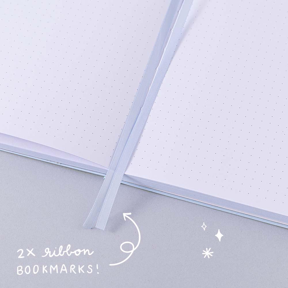 Close up of open Tsuki Four Seasons Winter Collector’s Edition Bullet Journal with two bookmark ribbons on light blue background