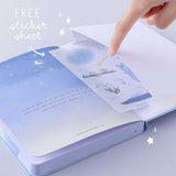Open back page pocket of Tsuki Four Seasons Winter Collector’s Edition Bullet Journal with free stickers sheet held in hand in light blue background