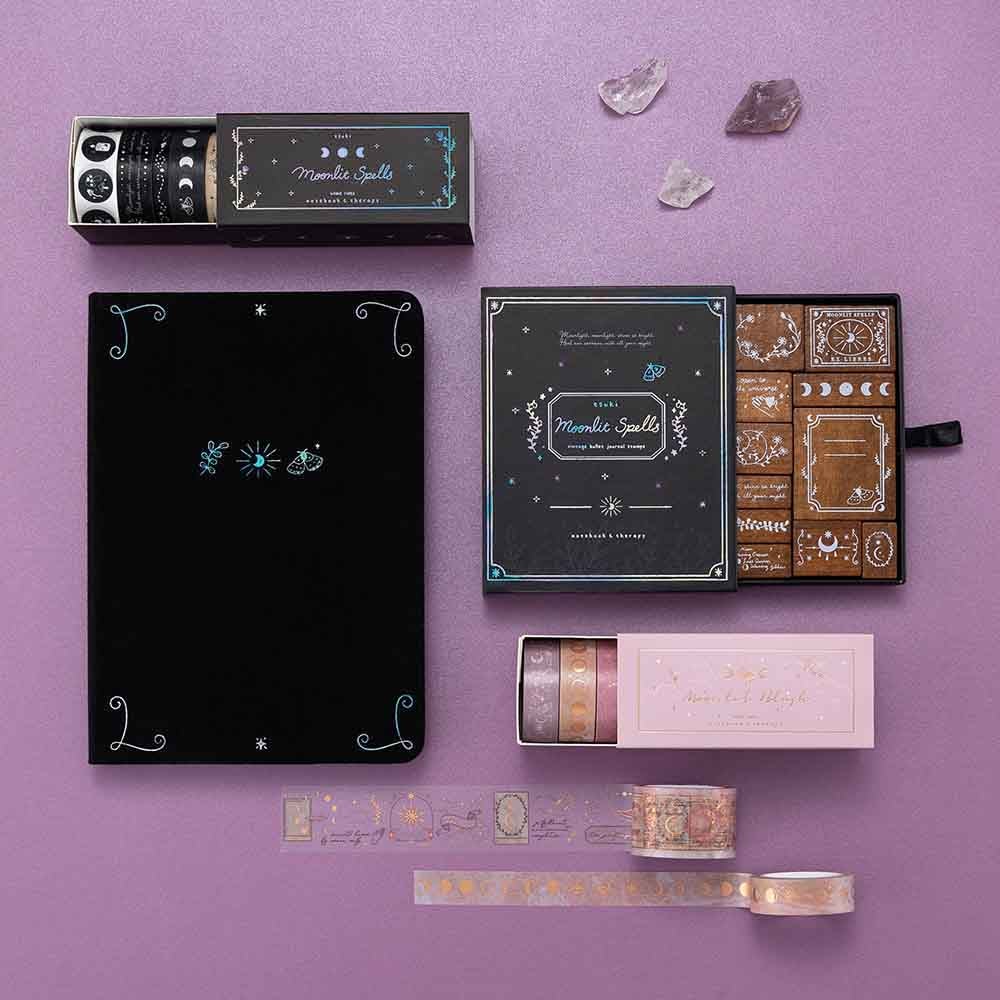 Tsuki ‘Moonlit Spells’ Bullet Journal Stamp Set with Tsuki ‘Moonlit Blush’ Washi Tapes and Tsuki ‘Moonlit Spells’ Washi Tapes on open bullet journal page with Tsuki ‘Moonlit Spell’ Limited Edition Holographic Bullet Journal on purple background