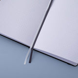 Deep black Tsuki Playful Orca limited edition bullet journal on open page with two bookmark ribbons on blue background