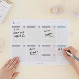 Tsuki Reusable Weekly Planner with dry erase marker held in hand with washi tape and sticky pen holder and calendar on buttermilk beige background