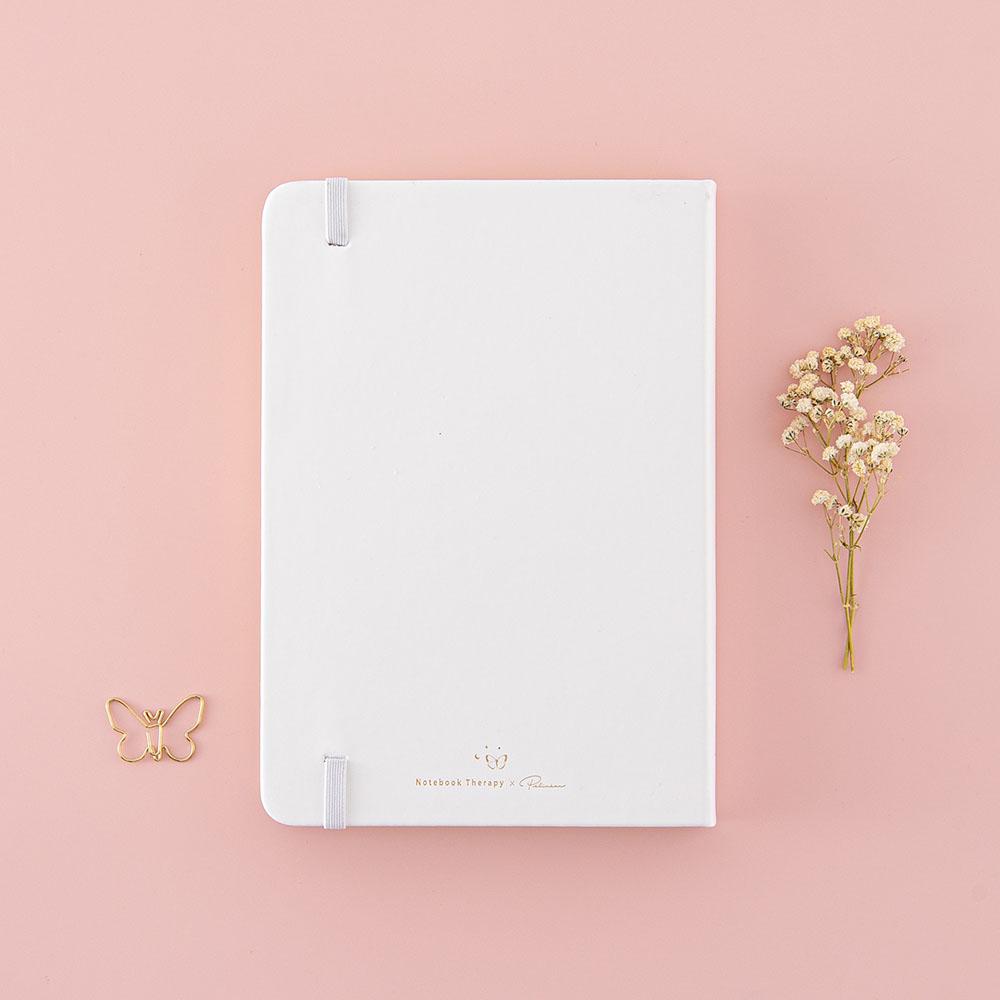 Back cover of Tsuki Cloud White ‘Flutter + Dream’ Limited Edition Bullet Journal by Notebook Therapy x Pelinkan with free butterfly bookmark gift with dried flowers on pastel pink background