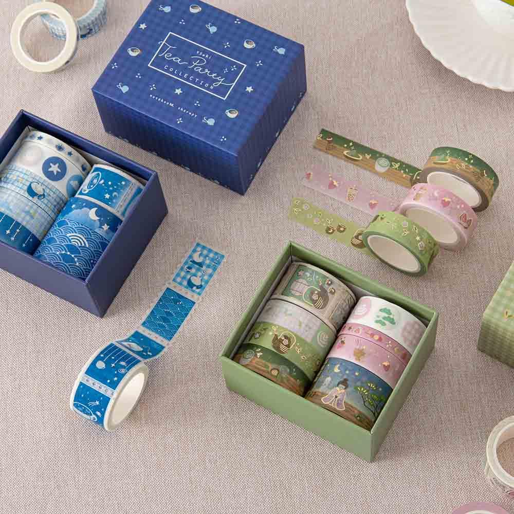 Close up of Tsuki ‘Matcha Ichigo’ Washi Tape Set and Tsuki ‘Cup of Galaxy’ Washi Tape Set with teacup saucer on linen covered table