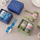 Close up of Tsuki ‘Matcha Ichigo’ Washi Tape Set and Tsuki ‘Cup of Galaxy’ Washi Tape Set with teacup saucer on linen covered table