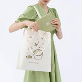 Tsuki ‘Matcha Matcha’ Tote Bag shown carried by model with Tsuki ‘Matcha Matcha’ Limited Edition Bullet Journal in light grey background
