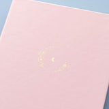 Close up of front cover of Tsuki ‘Lunar Blossom’ Limited Edition Bullet Journal on light blue background