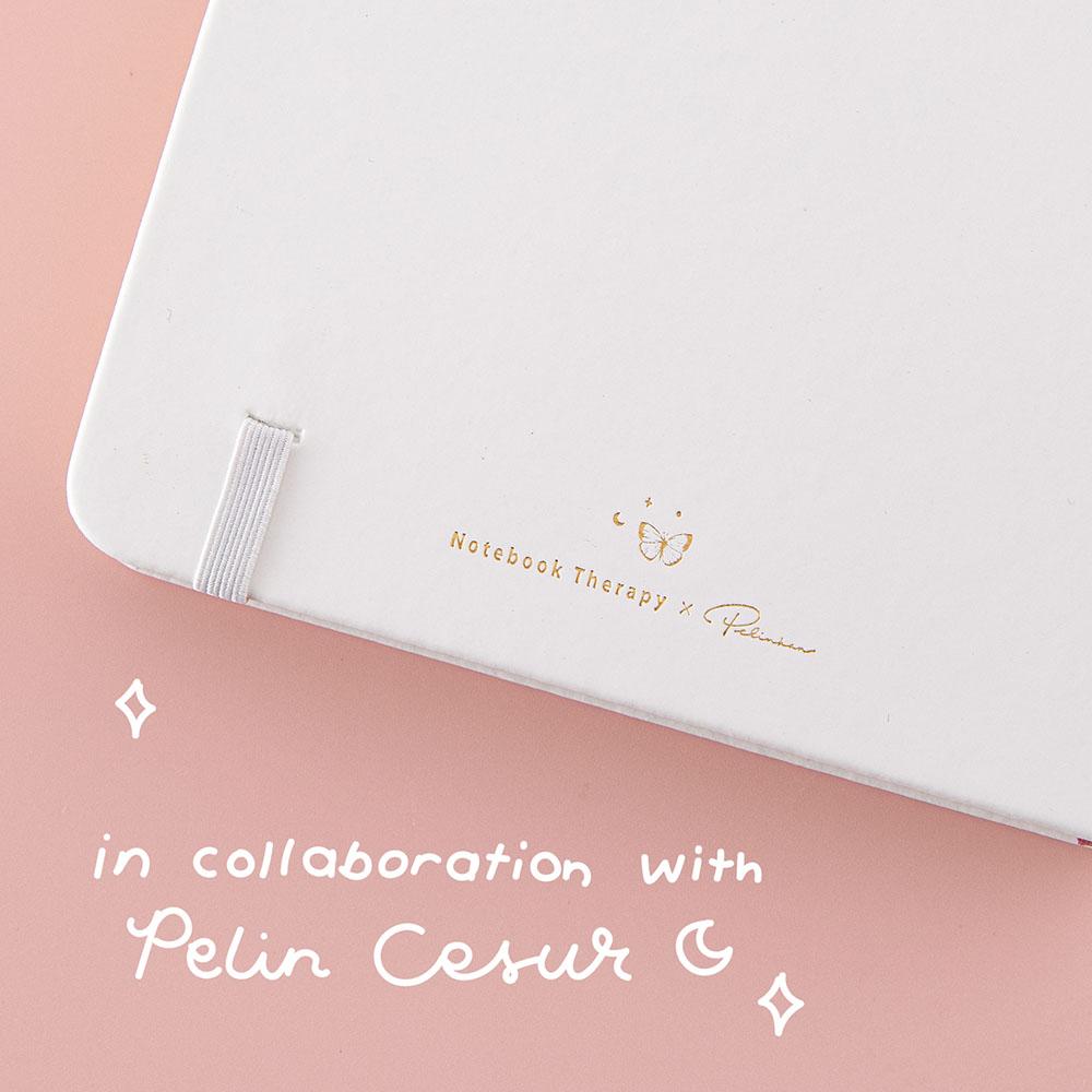 Close up of the back cover of Tsuki Cloud White ‘Flutter + Dream’ Limited Edition Bullet Journal by Notebook Therapy x Pelinkan on pastel pink background