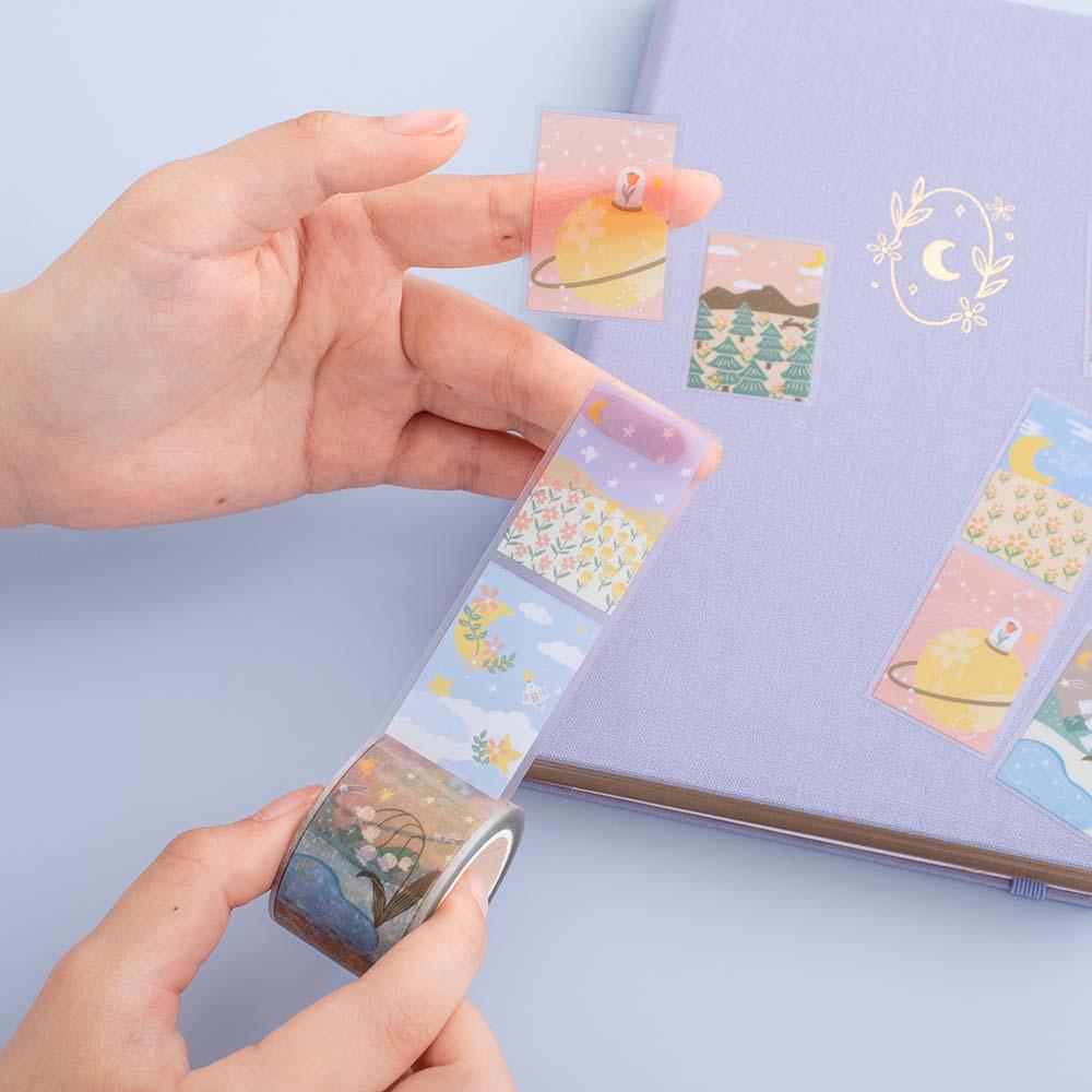 Tsuki ‘Moonflower’ Washi Stamp Tape held in hands with Tsuki ‘Full Bloom’ Limited Edition Bullet Journal on dusty blue background