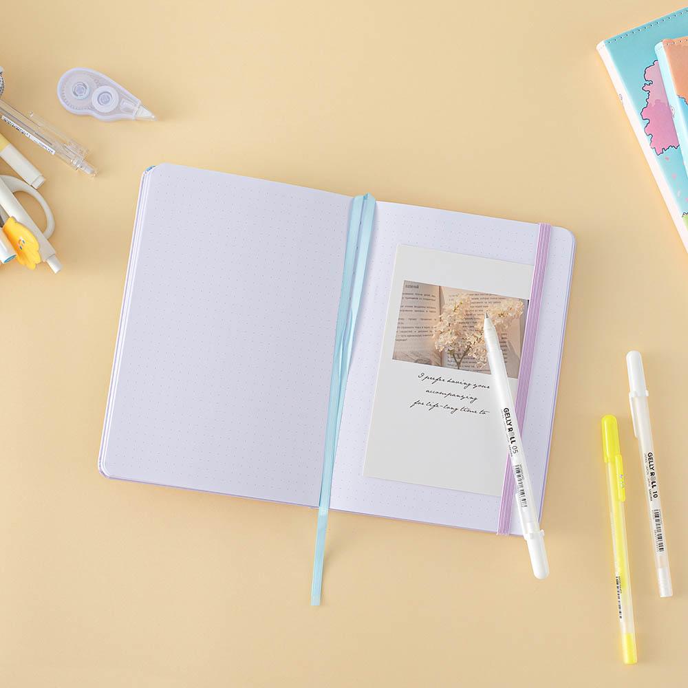 Tsuki Four Seasons: Summer Edition Bullet Journal designed with @milkkoyo on open page with pens and postcard and Tsuki Four Seasons: Spring Edition notebook on honey yellow background