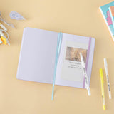 Tsuki Four Seasons: Summer Edition Bullet Journal designed with @milkkoyo on open page with pens and postcard and Tsuki Four Seasons: Spring Edition notebook on honey yellow background
