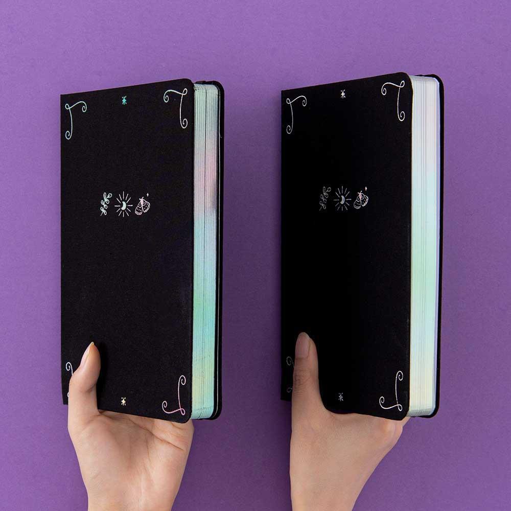 Tsuki ‘Moonlit Spell’ Limited Edition Holographic Bullet Journal with black or white pages held in hands at spine angle in purple background