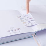 Close up of open back page pocket of Tsuki ‘Four Seasons: Autumn Edition’ Bullet Journal made with milkkoyo held in hand with free stickers sheet on lilac background