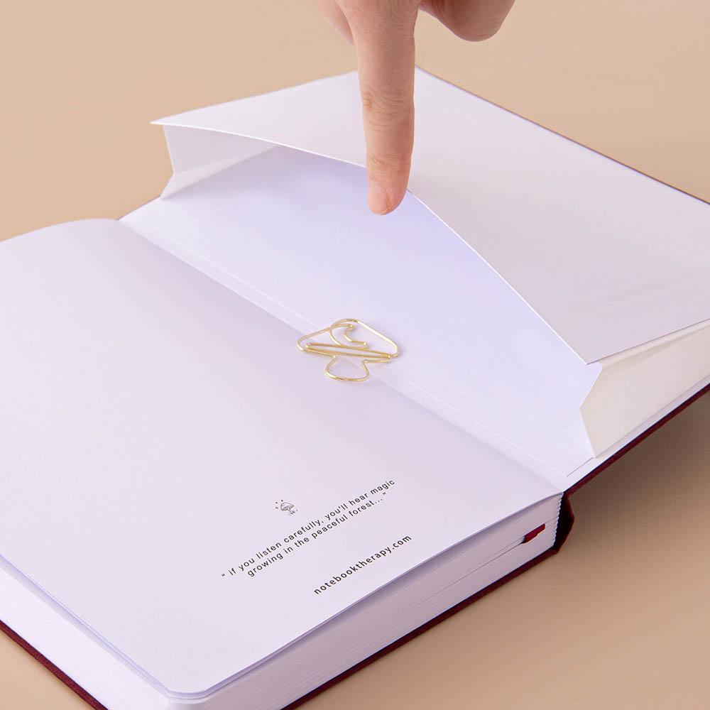 Open back page pocket of Tsuki ‘Kinoko’ Limited Edition Bullet Journal held in hand with free paperclip gift on beige background