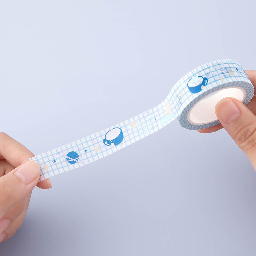 Close up of one Tsuki ‘Cup of Galaxy’ Washi Tape held in hands in light blue background