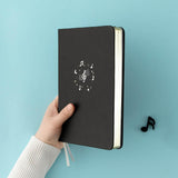 Tsuki Lunar Notes bullet journal in hand showing gold edge pages image in blue background