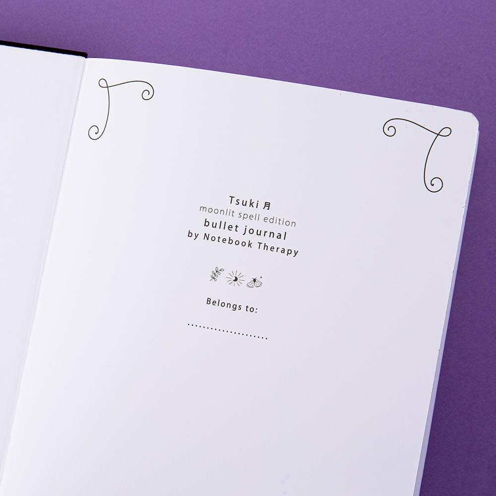 Close up of open front page of Tsuki ‘Moonlit Spell’ Limited Edition Holographic Bullet Journal on purple background