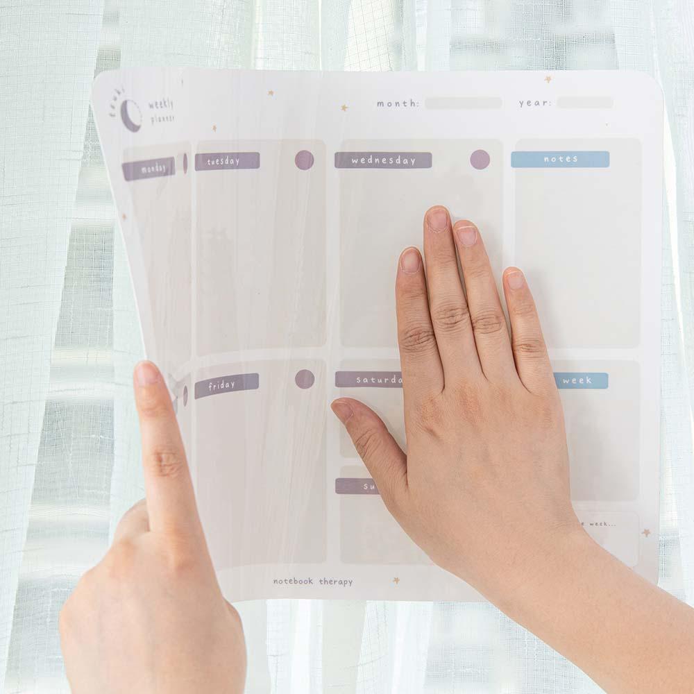 Tsuki Reusable Weekly Planner held in hands stuck onto glass window surface 
