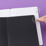Tsuki ‘Moonlit Spell’ Limited Edition Holographic Bullet Journals in black page and white page variations with free bookmark gift held in hand on purple background