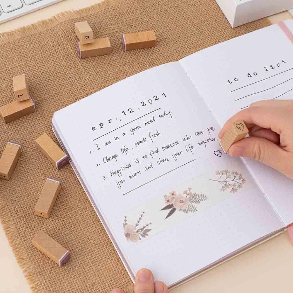 Tsuki Bullet Journal Typewriter Style Alphabet Stamps being used on open bullet journal with lettering on hessian mat on beige background