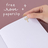 Close up of open Tsuki ‘Vintage Rose’ Limited Edition Bullet Journal with free rose paperclip held in hand in mauve background