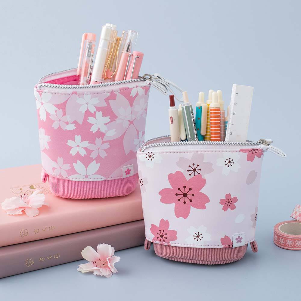 Tsuki 'Sakura Edition' Pop-Up Pencil Case in blush pink and petal pink with pens inside on Tsuki 'Sakura' Limited Edition Bullet Journal in Blush Pink and Petal Pink with sakura flowers in light blue background
