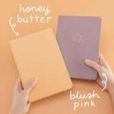 Tsuki Blush Pink ‘Bunny Blush’ Limited Edition Bullet Journal designed with Blossom Bujo with Tsuki Honey Butter ‘Bunny Blush’ Limited Edition Bullet Journal designed with Blossom Bujo held in hands in apricot background