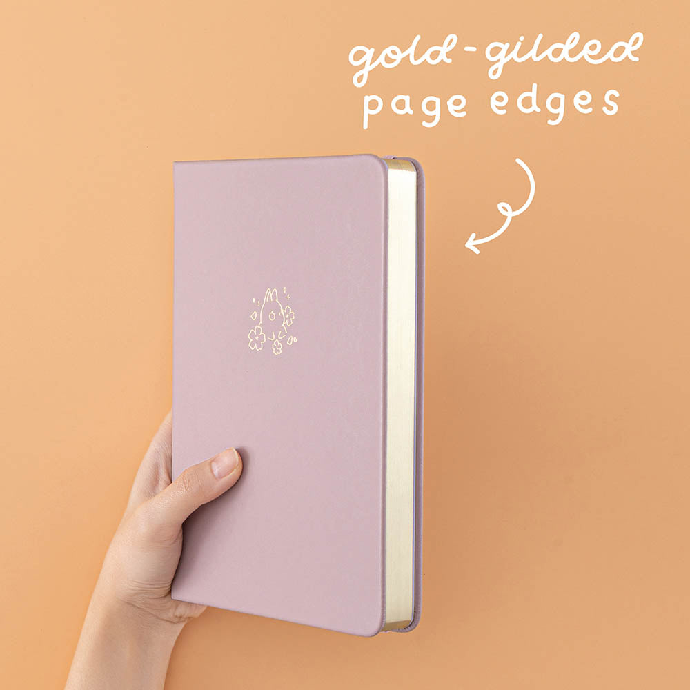 Tsuki Blush Pink ‘Bunny Blush’ Limited Edition Bullet Journal designed with Blossom Bujo with gold gilded page edges held in hands in lilac background