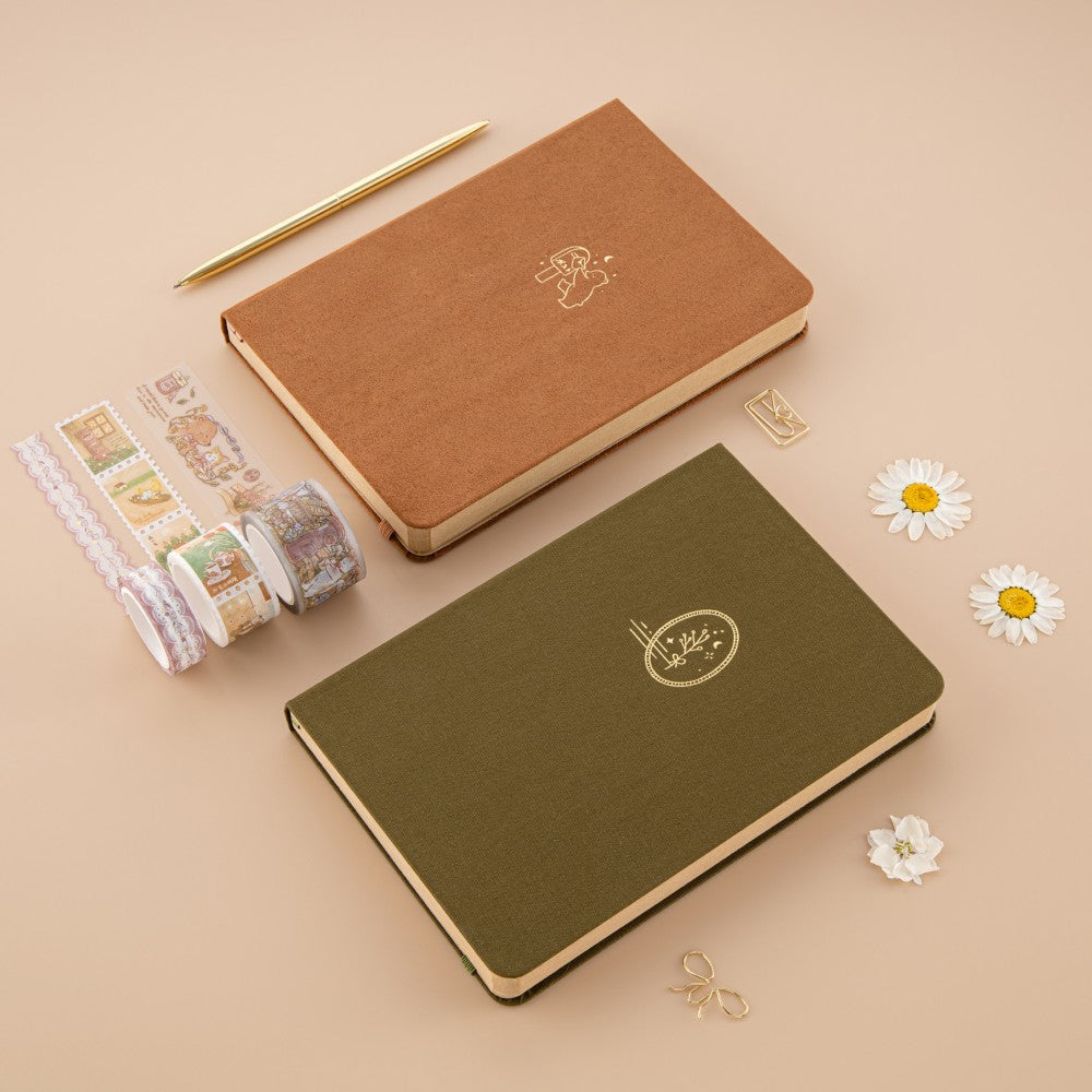 Brown velvet bullet journal and green linen bullet journal next to each other wish washi tapes and dried flowers around them
