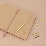 Kraft paper bullet journal laid flat with gold pen and gold love letter shaped paperclip on top