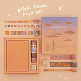 Flatlay of an opened Tsuki Golden Hour Bullet Journal Box Set contents of box includes an orange linen notebook, 6x washi tapes and 1x wooden rubber stamp