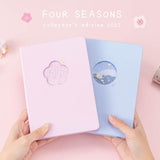 Tsuki Four Seasons: Spring Collector’s Edition 2022 Bullet Journal with Tsuki Four Seasons: Winter Collector’s Edition 2022 Bullet Journal held in hands with sakura blooms in light pink background