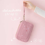 Tsuki ‘Sakura Journey’ Travel Pouch held in hands by detachable strap in pink background