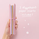 Tsuki ‘Sakura Journey’ Limited Edition Travel Notebook with three different paper inserts held in hand at spine angle in pink background
